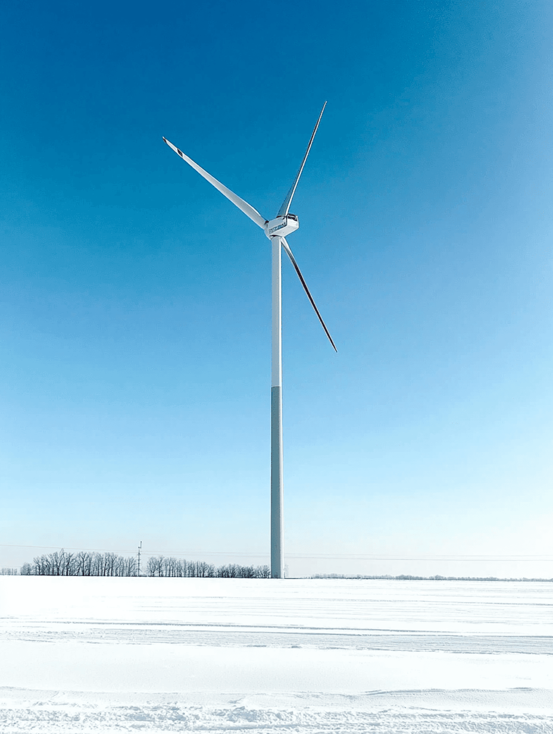 A wind turbine under a clear blue sky above a snowy field